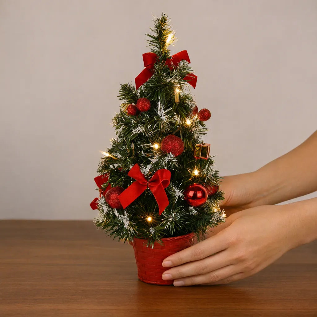 Hands setting a red mini Christmas tree with lights on a wooden desk