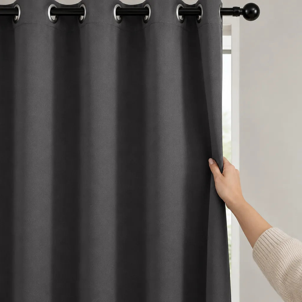 Hand pulling a grey eyelet blackout curtain closed across a bedroom window