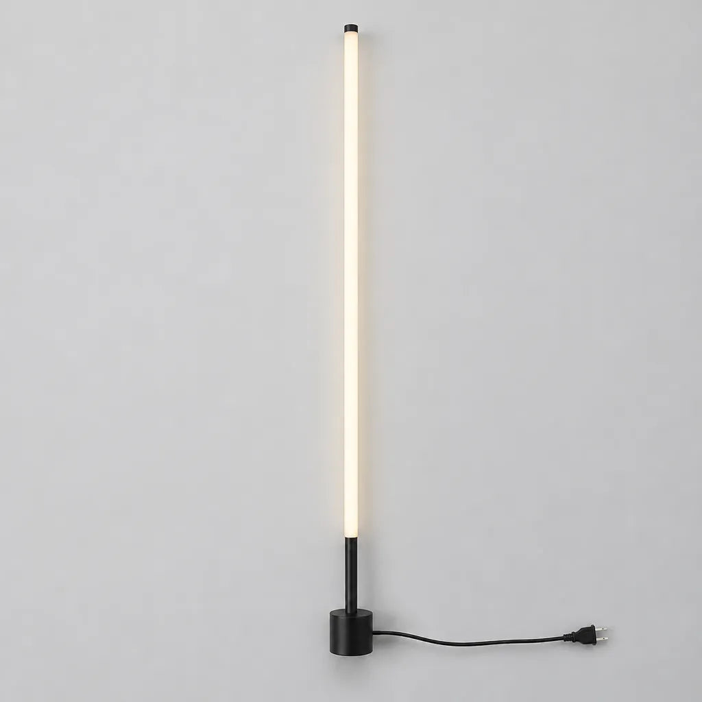 Slim black LED floor lamp with round base and power cord laid flat on a grey surface