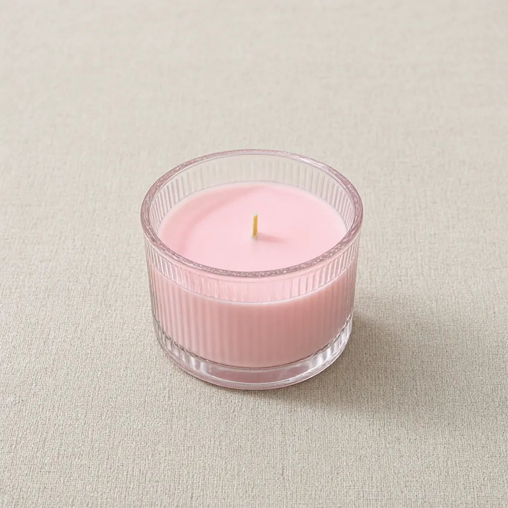 Single pink scented candle in a ribbed glass jar with a wooden wick on a linen surface