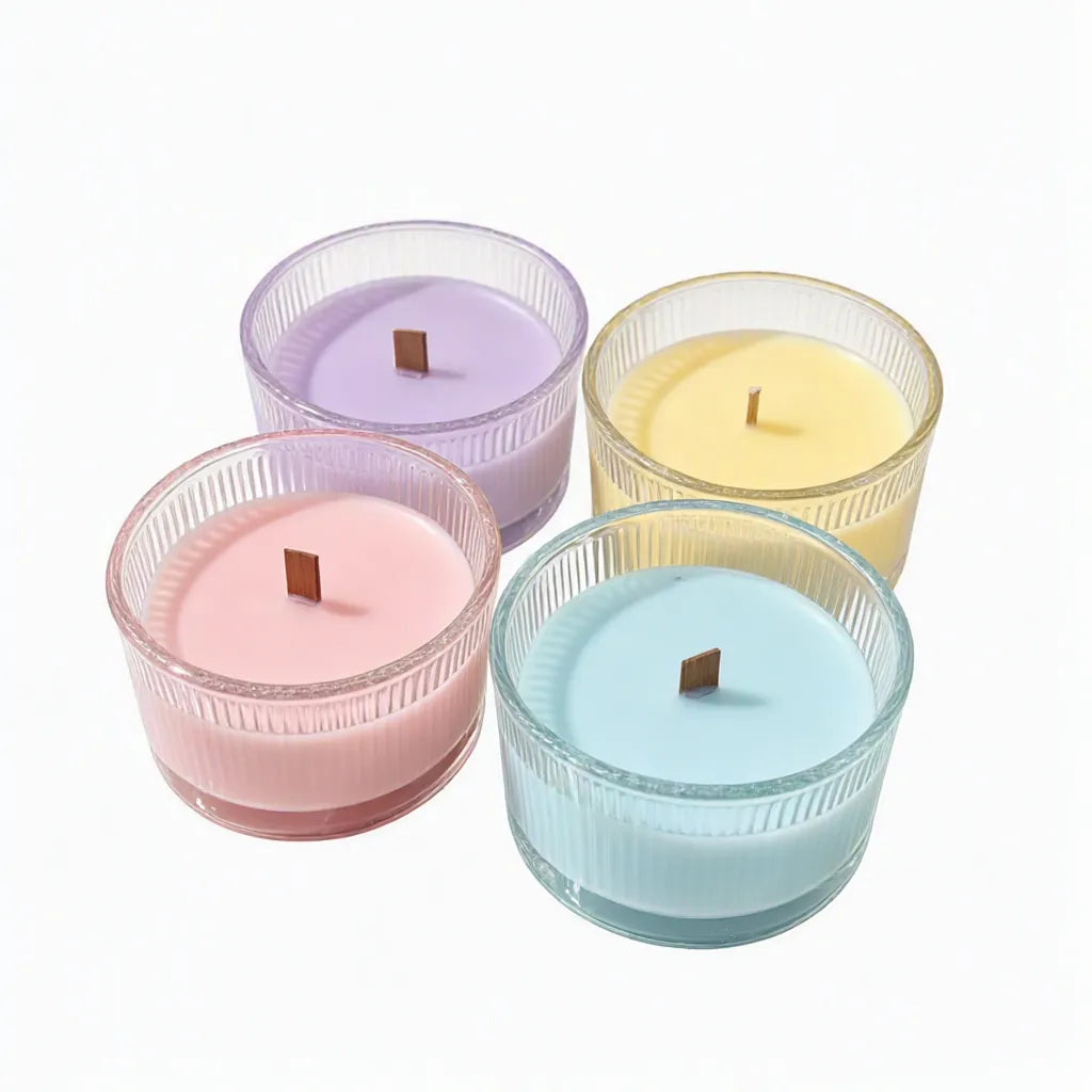Four pastel scented candles in ribbed glass jars with wooden wicks on a white background