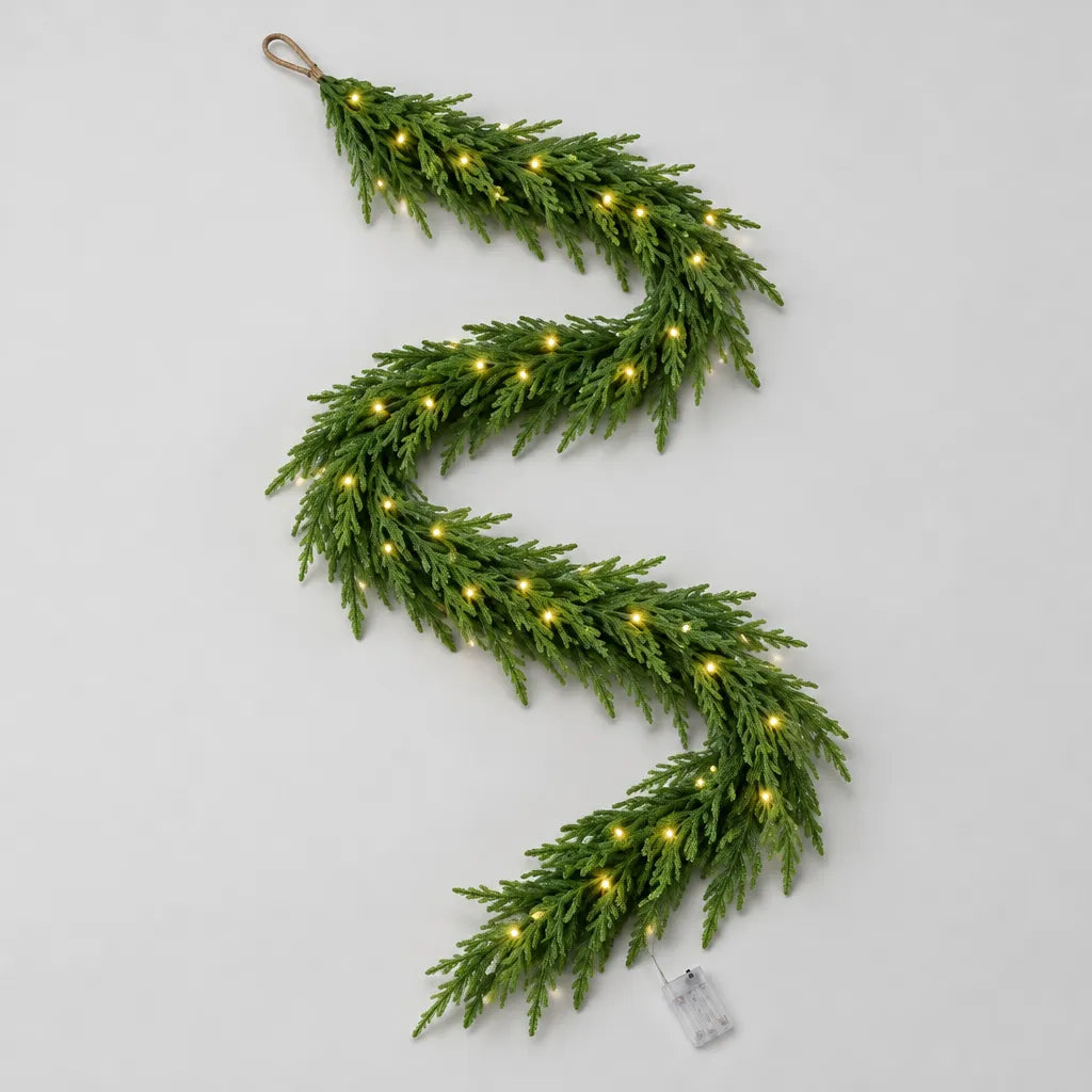 Norfolk pine Christmas garland with lights and battery box laid out on a grey surface