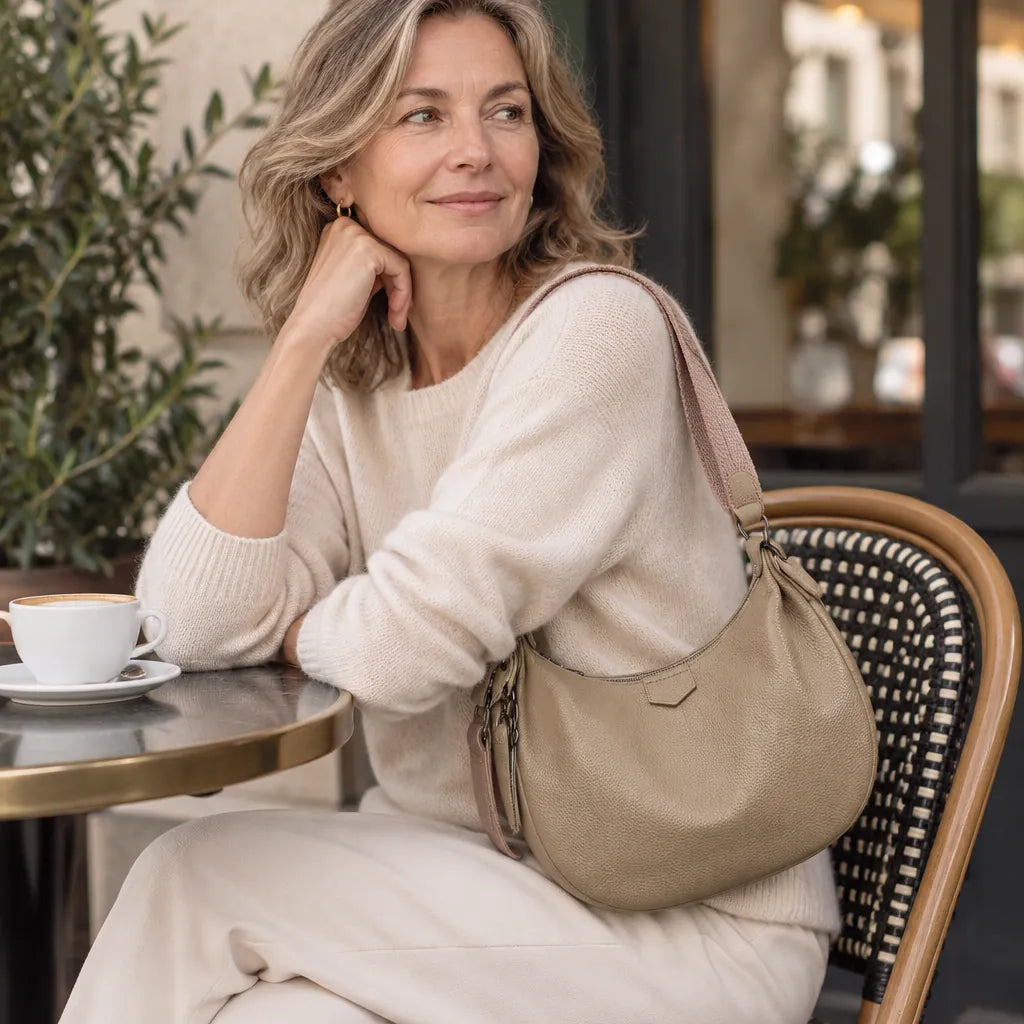Woman at a cafe table with a khaki leather shoulder bag on her shoulder