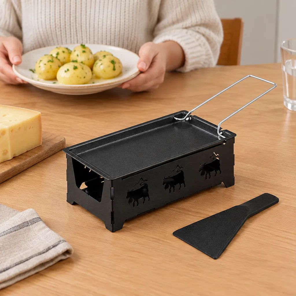 Schwarzes Raclette Set mit Teelichtern auf einem Tisch neben einem Stück Käse und einem Teller Pellkartoffeln