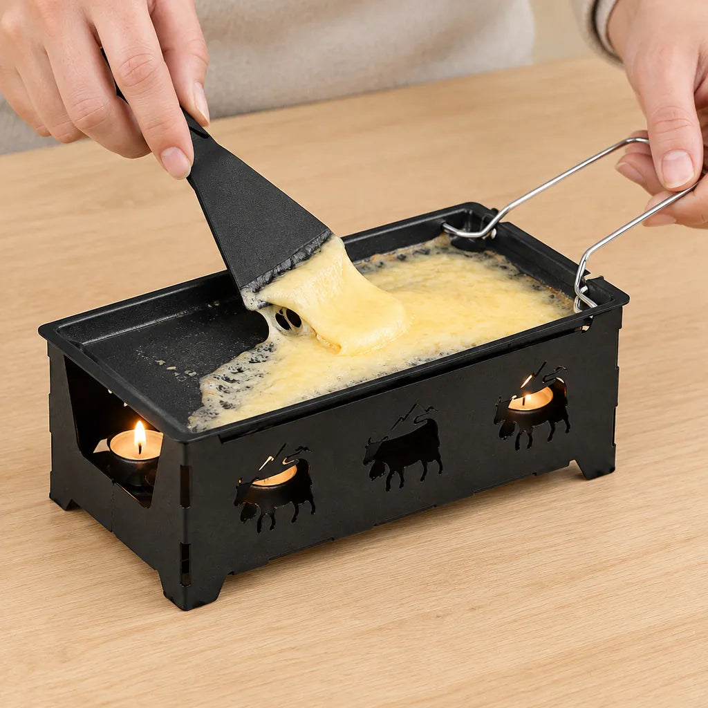 Hands scraping melted raclette cheese from the pan of a mini raclette oven set heated by tea lights