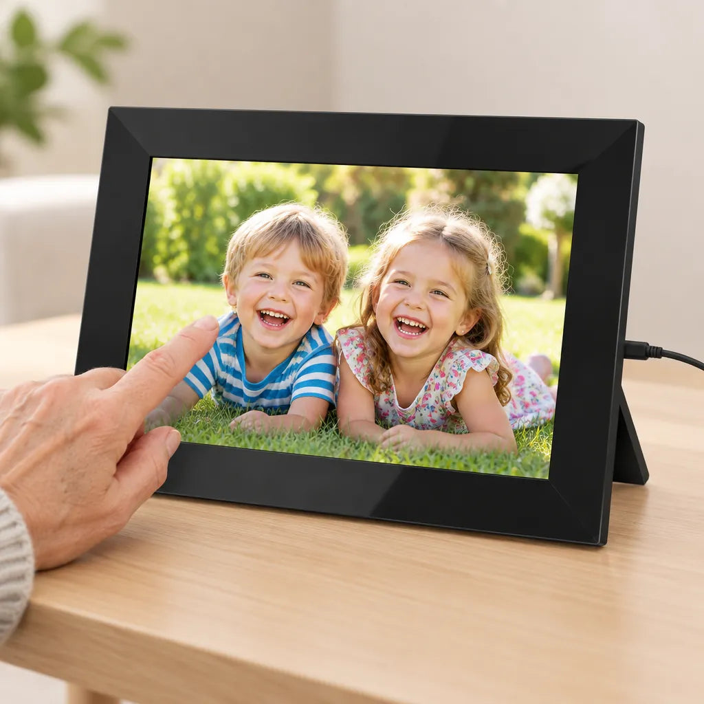 Hand swiping a photo of two smiling kids on a black WiFi digital picture frame on a wooden side table
