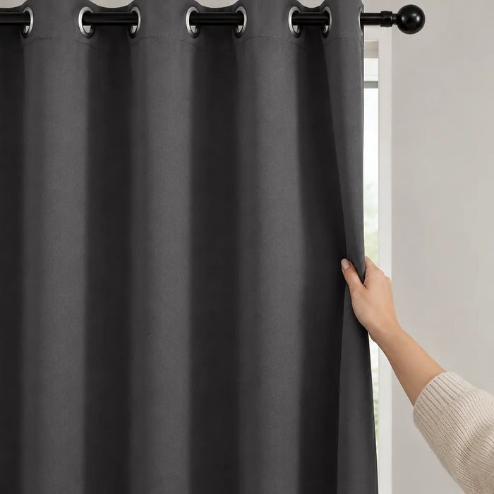 Hand pulling a grey eyelet blackout curtain closed across a bedroom window