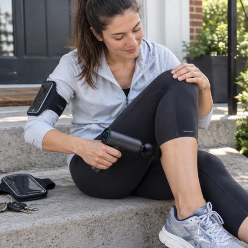 Runner sitting on her front steps using a mini massage gun on her calf