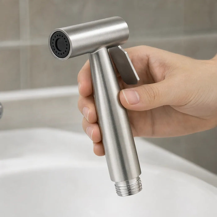 Hand gripping a stainless steel handheld bidet sprayer over a white sink