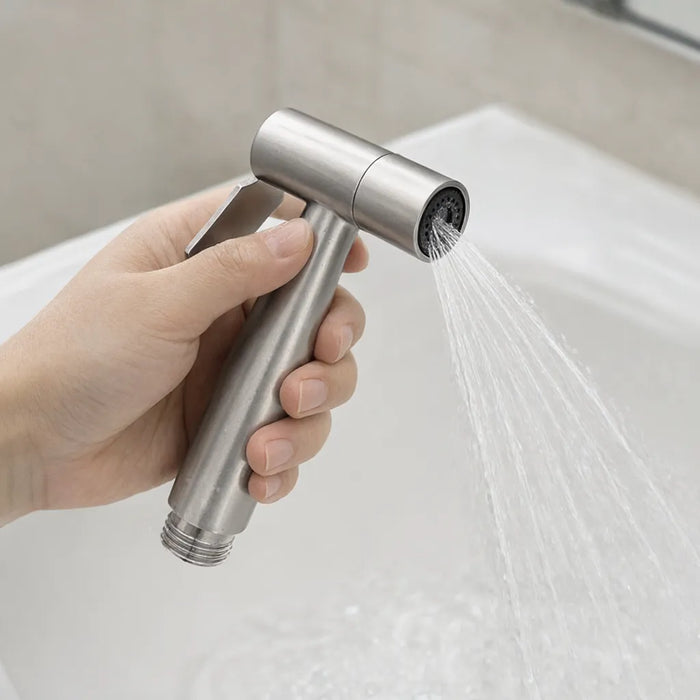 Hand squeezing the trigger of a handheld bidet sprayer with water spraying into a sink