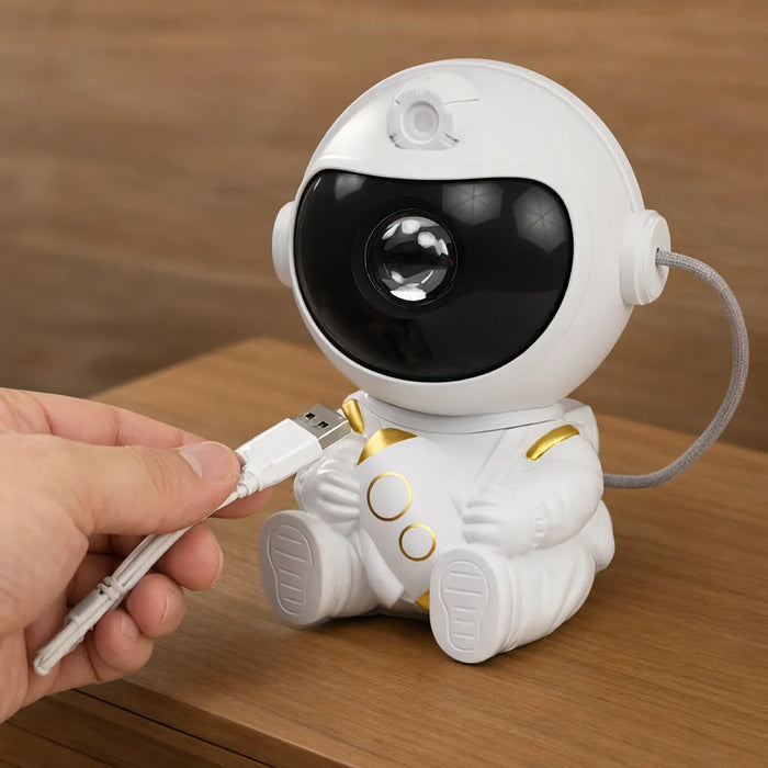 Mano conectando un cable USB al proyector de astronauta sobre una mesa de madera