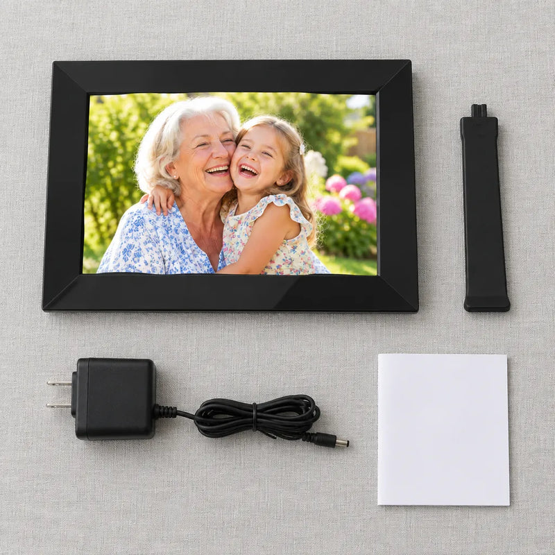 Black digital picture frame, stand, power adapter and user manual laid out on linen