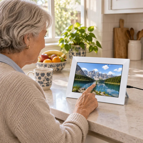 Grandmother in her kitchen swiping a white touch screen picture frame showing a mountain lake