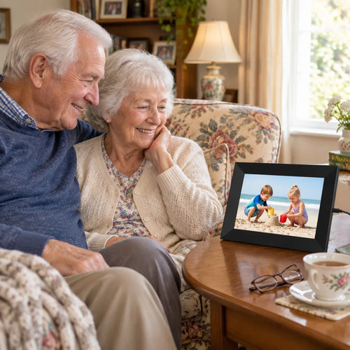 Grandparents on the sofa smiling at a black digital picture frame showing their grandchildren