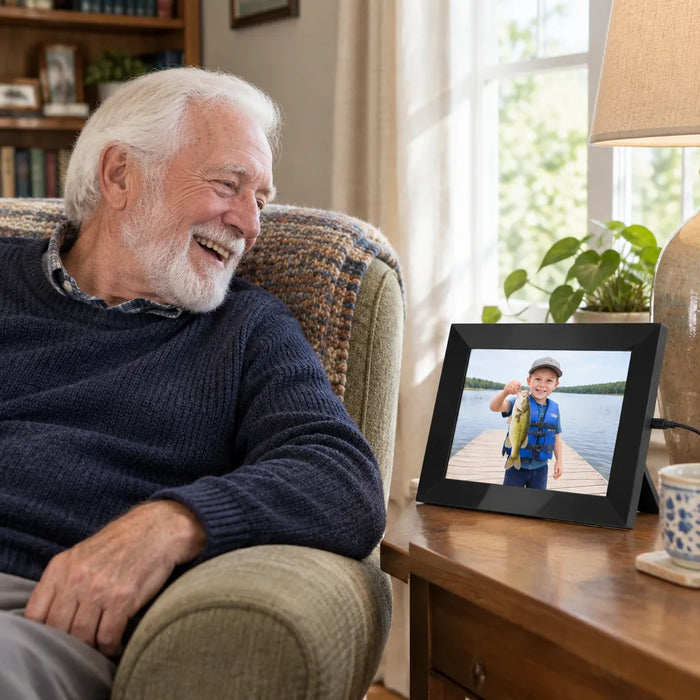 Grandfather laughing at a photo of his grandson on a smart digital picture frame beside his armchair