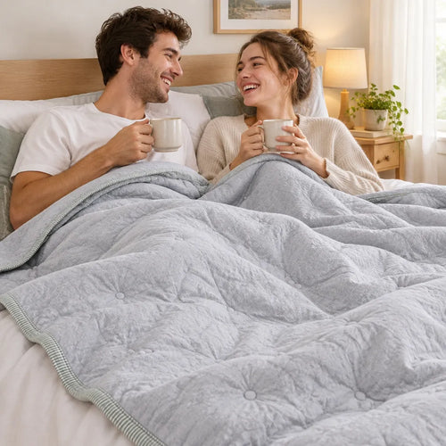 Paar lacht mit Kaffee im Gästebett unter einer leichten Sommerdecke aus Baumwolle