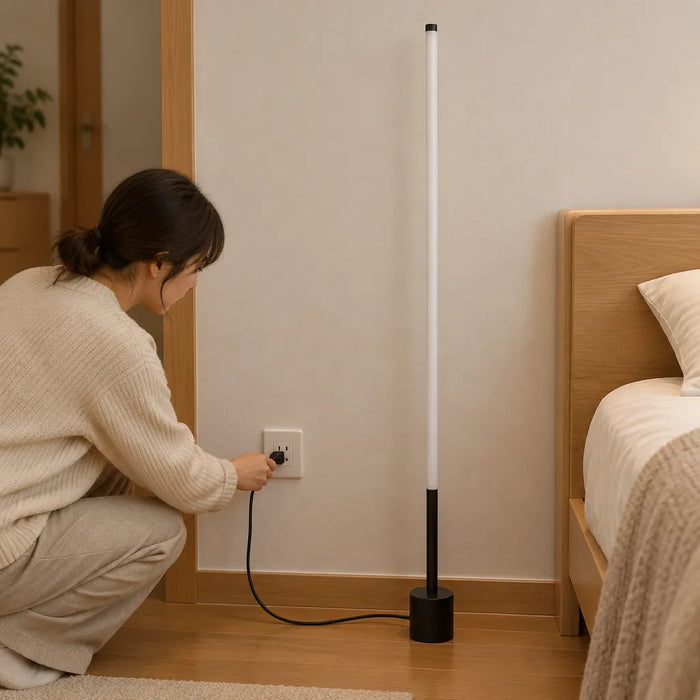 Femme qui branche une lampe sur pied LED noire et mince près d'un lit