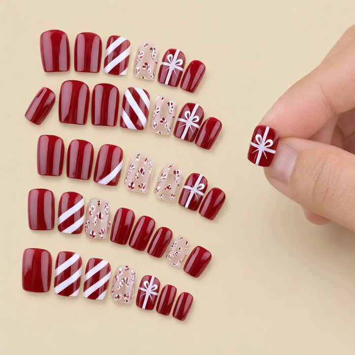 Fingers pressing a red gift bow press-on nail onto a natural nail, christmas press on nails