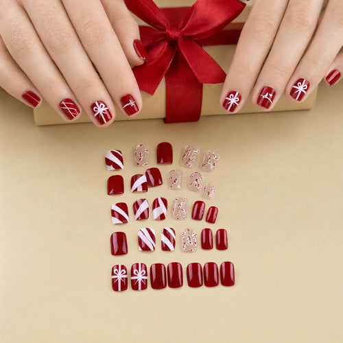 Hands tying a red ribbon on a christmas gift, wearing short red press on christmas nails
