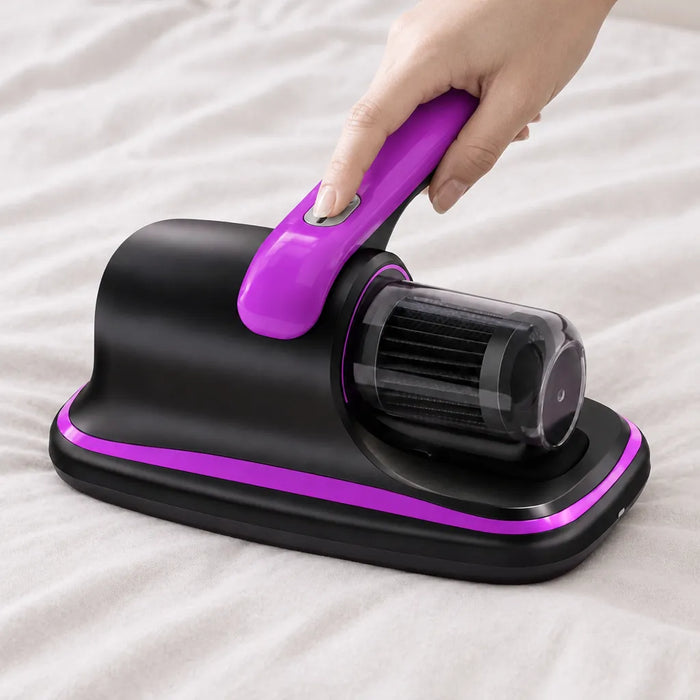 Hand pressing the power button on a handheld mattress vacuum resting on a bed