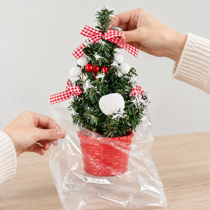 Hände nehmen einen Mini-Weihnachtsbaum im roten Topf aus dem transparenten Beutel