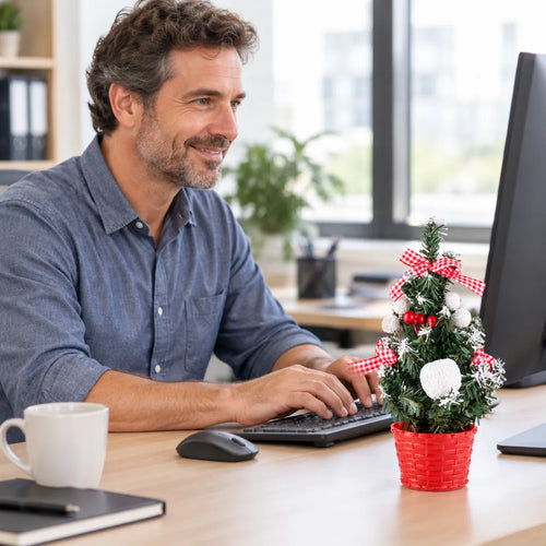 Mann tippt am Bürotisch neben einem Mini-Weihnachtsbaum im roten Topf