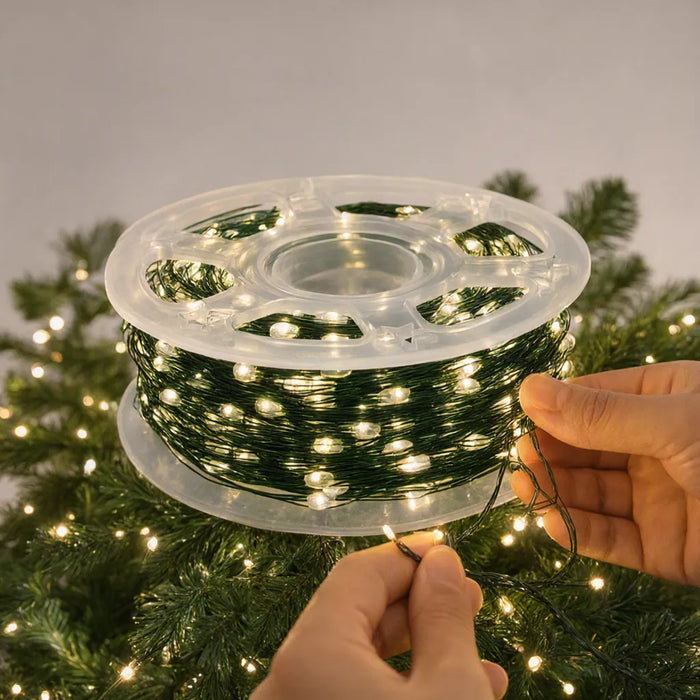 Hands winding warm white LED string lights around a Christmas tree branch