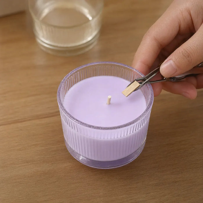 Hands trimming the wooden wick of a lavender scented candle in a ribbed glass jar