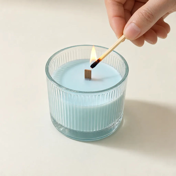 Lighting the wooden wick of a light blue scented candle with a match