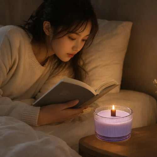 Young woman reading in bed with a lit lavender scented candle on the bedside table