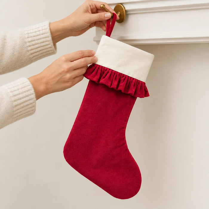 Mains suspendant un bas de Noël rouge en velours par sa boucle à un crochet