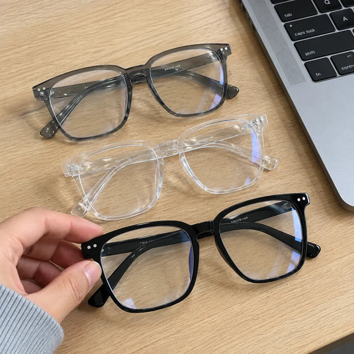 Hand picking the black pair from three square glasses on a desk next to a laptop