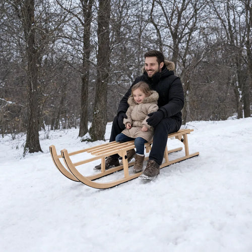 Vater und kleine Tochter sitzen auf einem Holzschlitten an einem verschneiten Parkhang