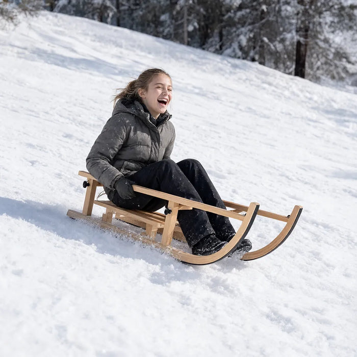 Lachendes Mädchen fährt mit dem Holzschlitten einen verschneiten Hang hinunter