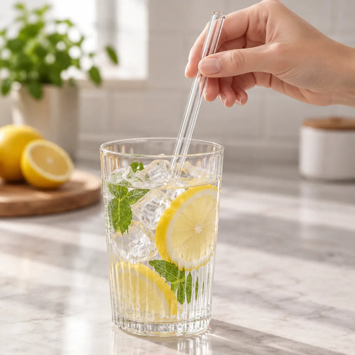 Main plongeant une paille en verre dans un verre d'eau citronnée glacée