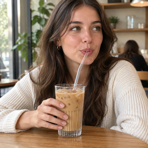 Jeune femme buvant un café glacé avec une paille en verre coudée dans un café