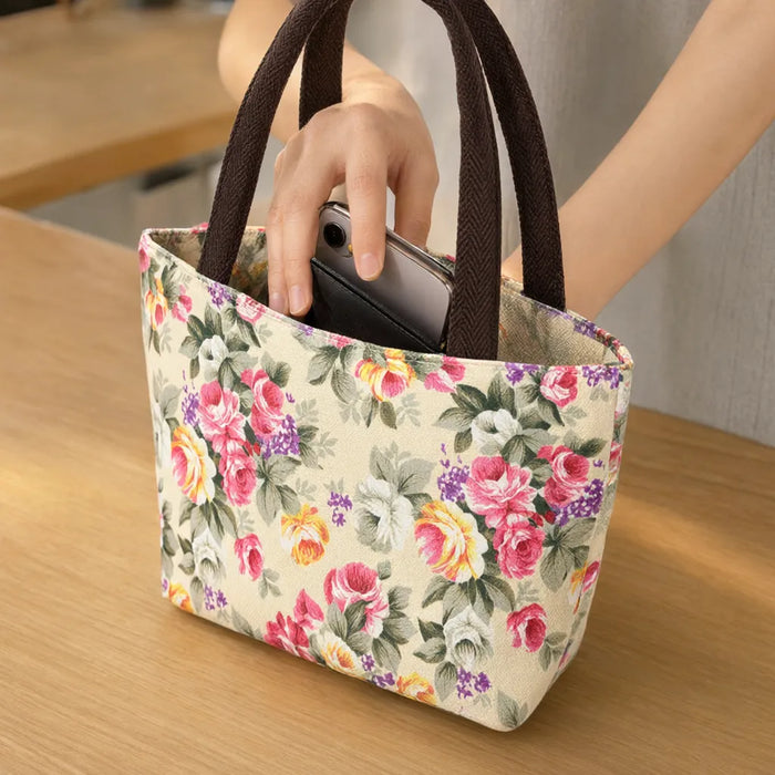 Hand slipping a phone into a small canvas tote bag with a rose print