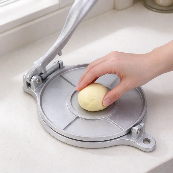 Hand placing a ball of dough on the plate of a silver tortilla press