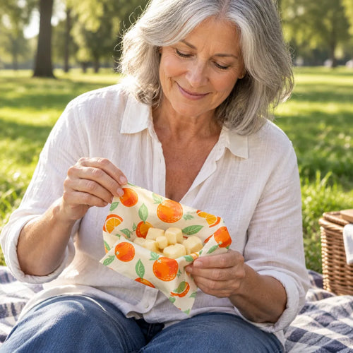 Woman at a picnic opening a small orange print beeswax wrap with cheese cubes