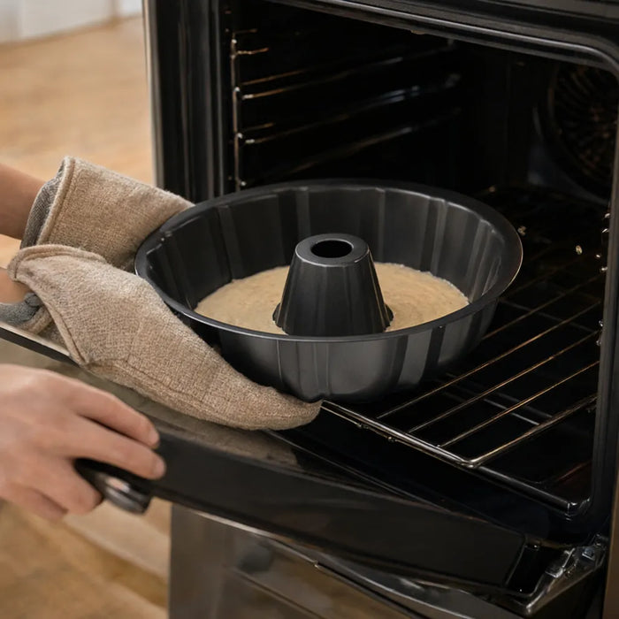 Manos con guantes de cocina metiendo al horno un molde para rosca con masa