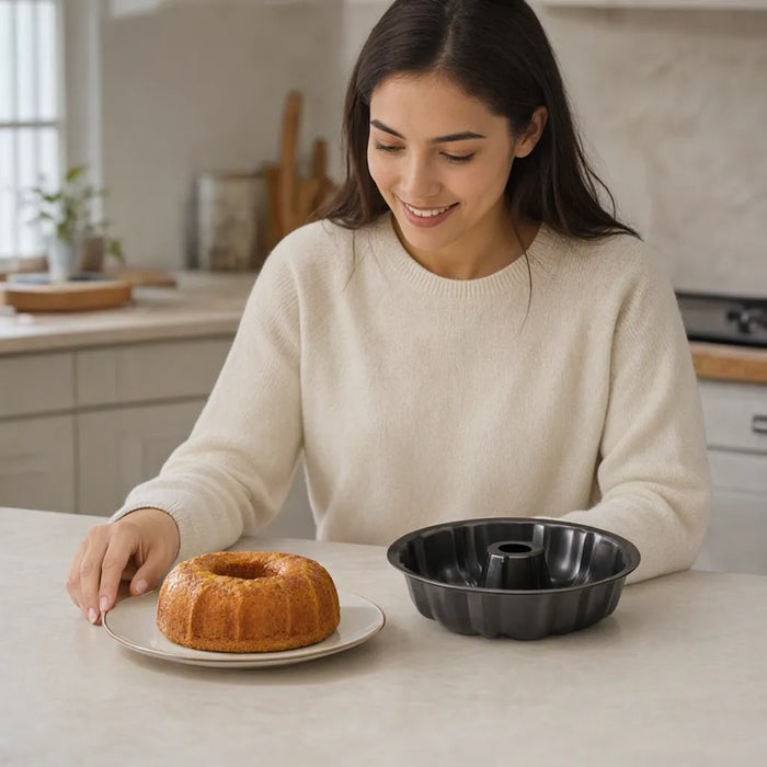 Mujer sonriendo en una mesa con una rosca dorada junto a su molde bundt negro