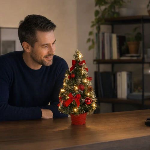 Hombre sonriendo ante un árbol de Navidad de escritorio con luces