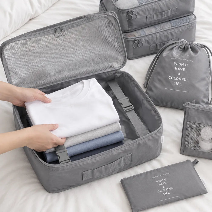 Hands laying folded T-shirts into an open grey packing cube with inner buckle straps