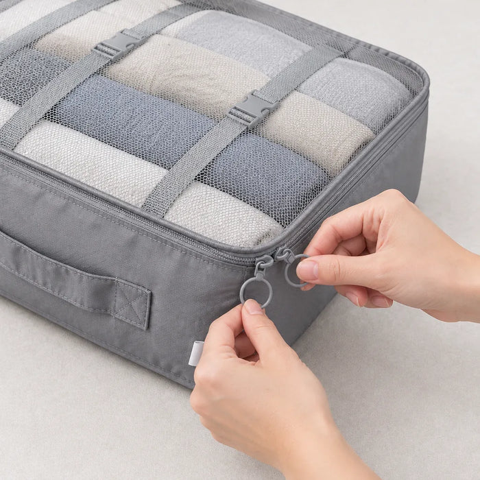 Hands closing the two-way zip of a full grey packing cube with mesh top