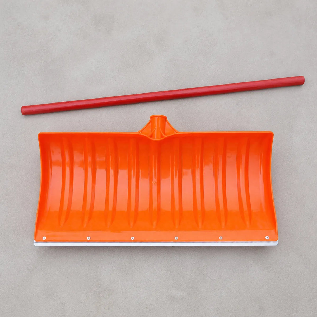 Orange snow shovel blade with a separate red wooden handle laid out on a grey surface