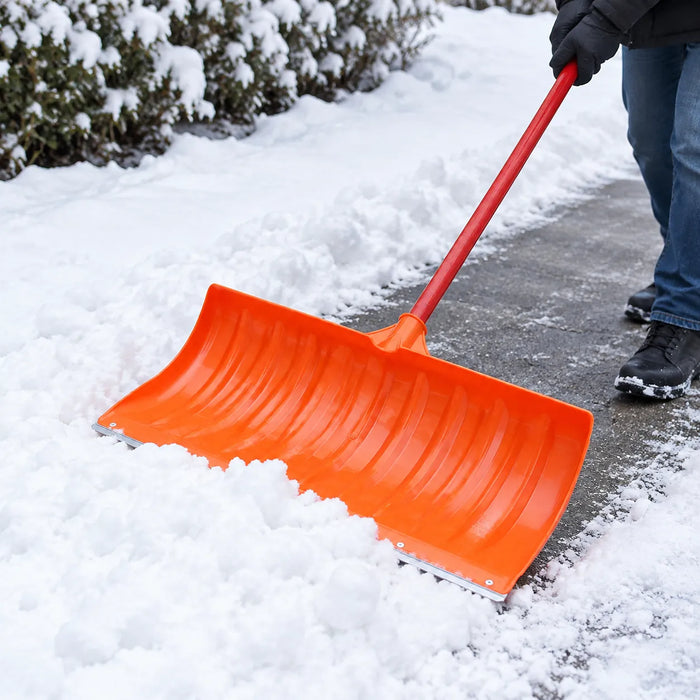Oransje snøskuffe skyver en bred stripe snø langs en hagesti