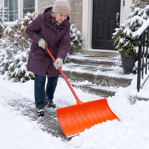 Kvinne måker snø av inngangstrappen med en oransje snøskuffe