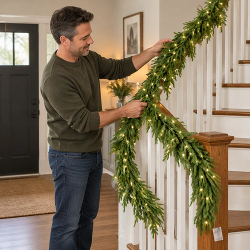 Man wrapping a lit Christmas garland around a staircase banister