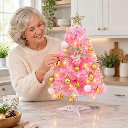 Smiling woman decorating a mini pink Christmas tree on a kitchen counter