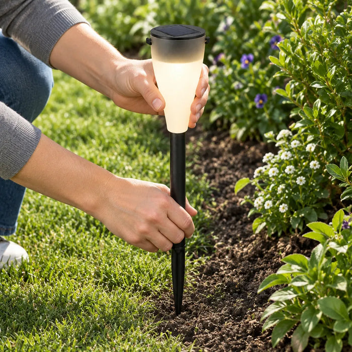 Manos clavando una luz solar para camino en la tierra de una jardinera